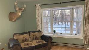 Ein gemütliches Wohnzimmer mit großem Fenster, einem aufgehängten Hirschgeweih und einem Sofa im Vintage-Stil.