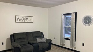 Ein Wohnzimmer mit einer schwarzen Ledersofa, einer Wanduhr und einem Fenster mit Vorhängen.