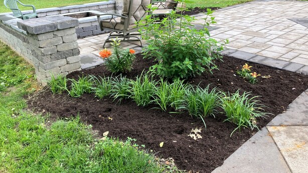 Eine Terrasse mit Steinkamin, Sitzgelegenheiten im Freien und einem Gartenbereich mit verschiedenen Pflanzen und Blumen.
