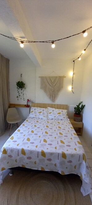 Une chambre bien rang ée, avec un lit, une table de chevet, une chaise et des plantes suspendues.