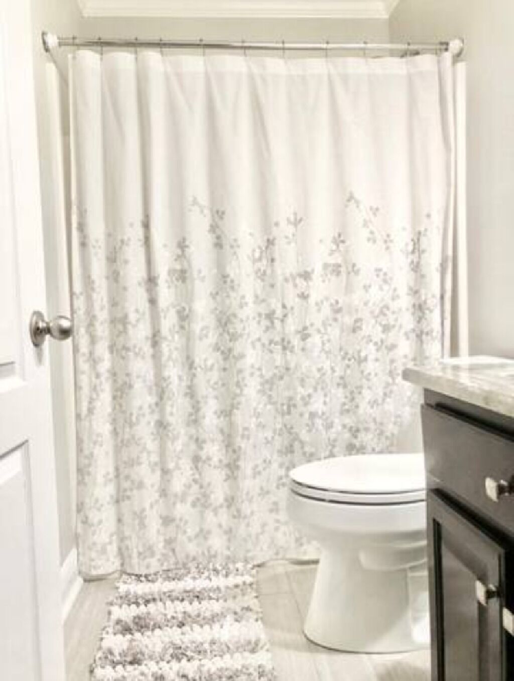 Un baño con inodoro, cortina de ducha con estampado floral y una alfombra en el suelo.