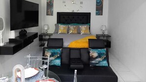 A modern bedroom with a large bed, a flat-screen TV, a ceiling fan, and artwork on the walls. - Serenity's Condo 2 Bedroom Apartment (Montego Bay)