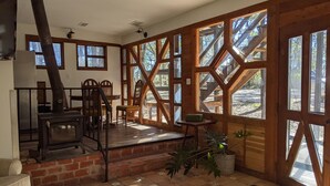 A rustic interior with a fireplace, wooden furniture, and large windows offering views of the outdoors. - Rustic modern cabin surrounded by trees and large yard 25 miles from Waco/Temple (Lott)