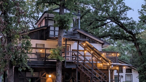 A multi-story building with a staircase leading to a balcony, surrounded by trees. - Rustic modern cabin surrounded by trees and large yard 25 miles from Waco/Temple (Lott)