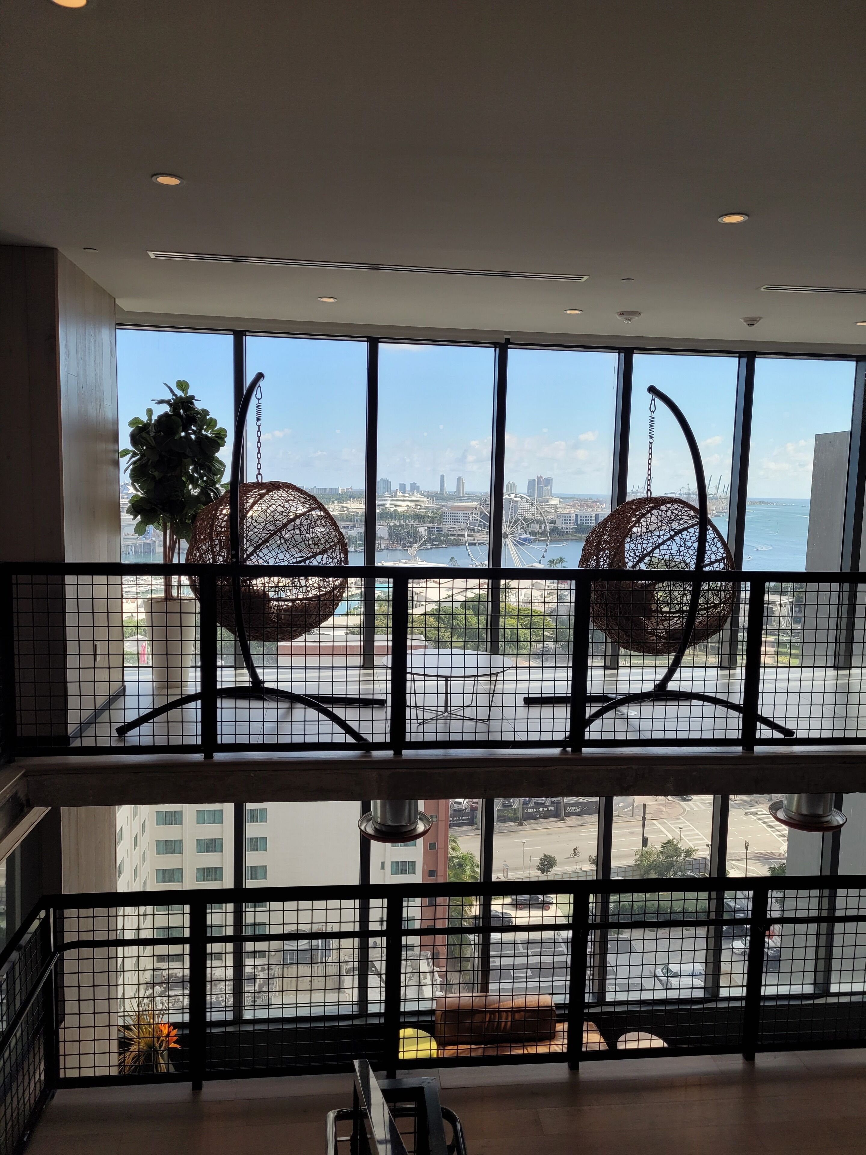 Camera d'hotel di un grattacielo con ampie finestre che offrono vista sulla città, un balcone con ringhiera e una sedia a dondolo.