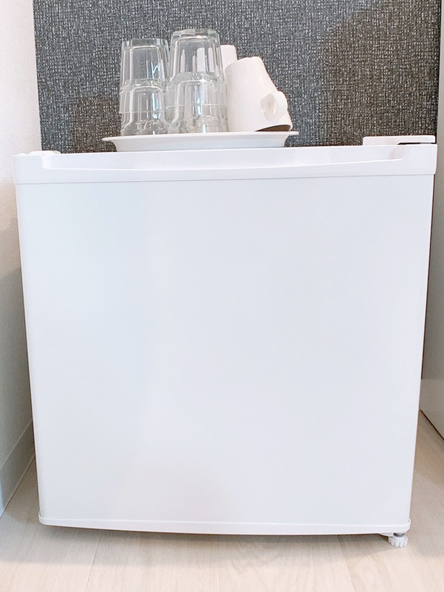 A white storage unit with a flat surface and a handle, containing several clear glasses and a white object.
