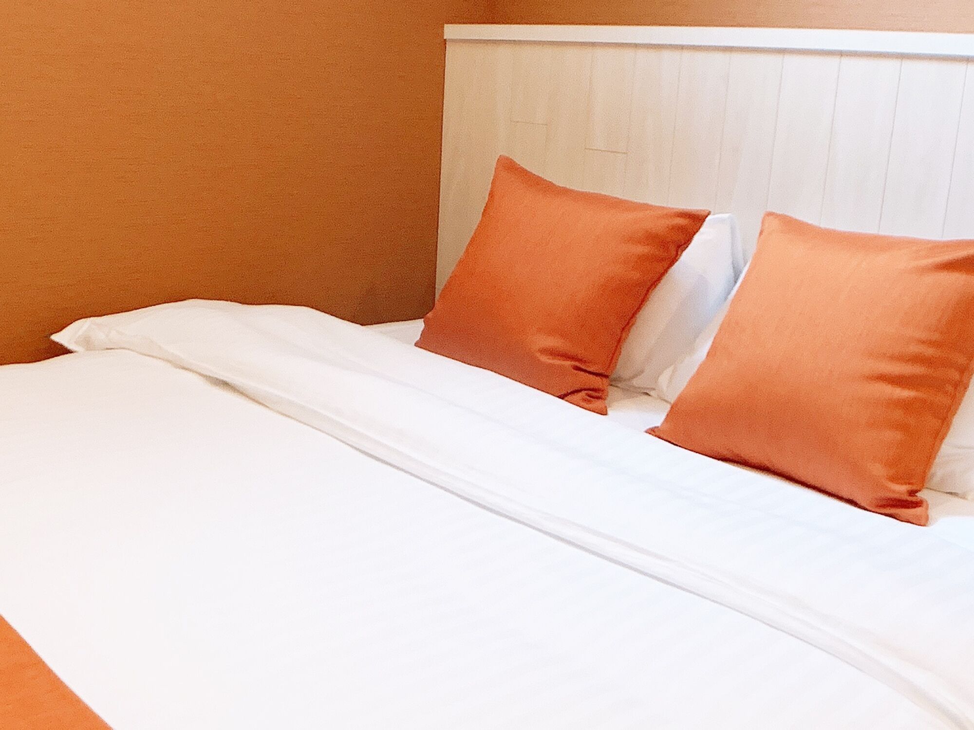 Un lit avec une literie blanche et deux oreillers orange.