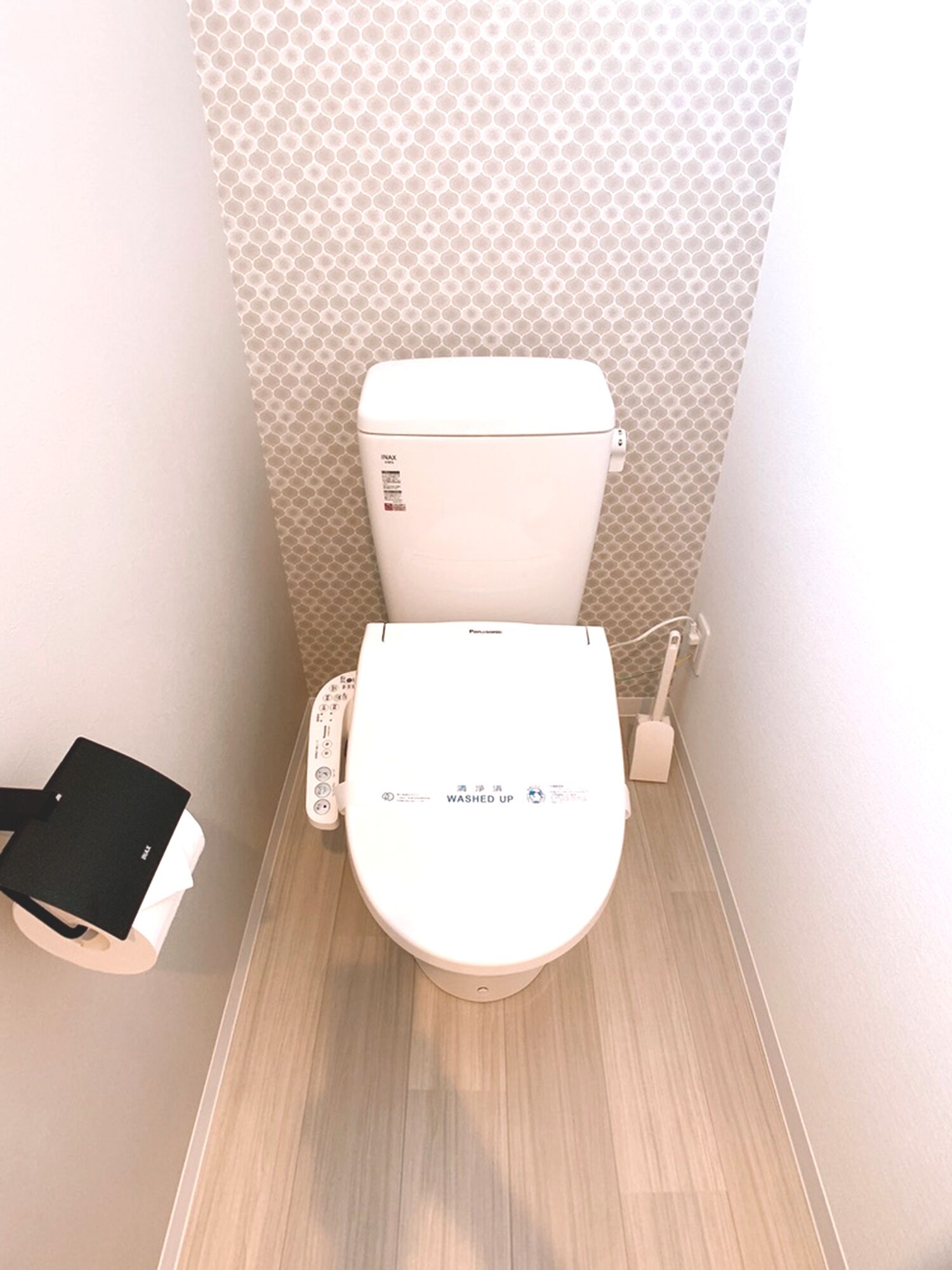 A modern toilet with a control panel, a toilet brush, and a tissue holder.