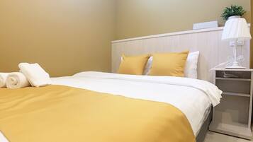 Una cama bien hecha con una colcha amarilla y blanca, una almohada blanca y una toalla blanca enrollada a un lado.
