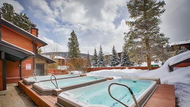 A pool area with two hot tubs, surrounded by snow and trees.