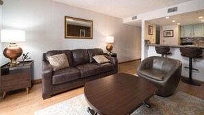 A modern living room with a brown leather sofa, a wooden coffee table, and a bar area with stools.