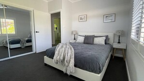 Une chambre moderne avec un grand lit, un dressing et une vue sur le paysage urbain par la fenêtre.