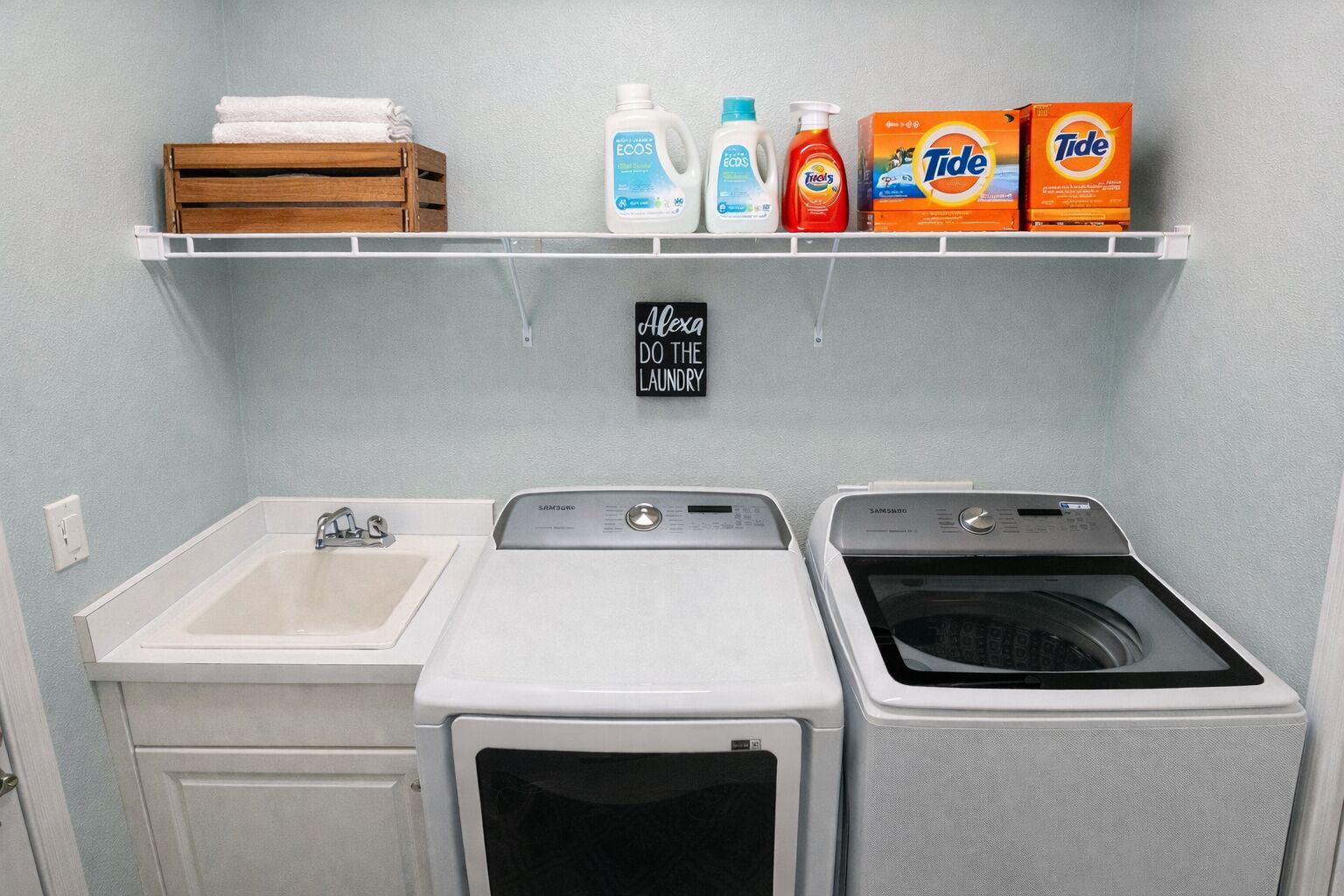 A laundry room with a sink, two washing machines, and a shelf with laundry supplies.
