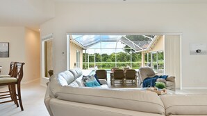 A spacious living area with a large window, a ceiling fan, and a dining area with chairs and a table. - LUXURY Villa ALEXA Naples

Modern Voice controlled Villa with SALT WATER POOL (Naples)