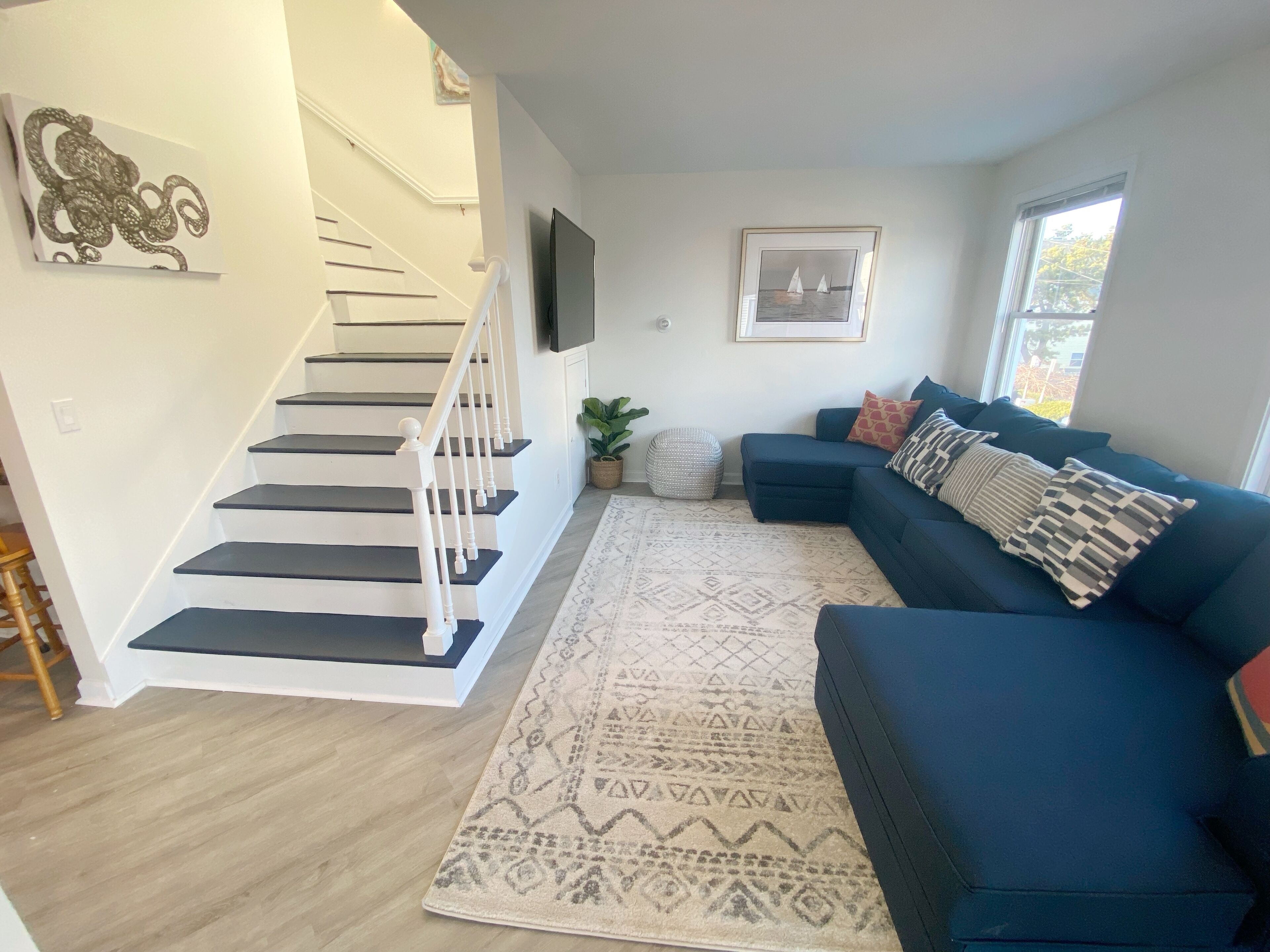A living room with a staircase, a blue sofa, a patterned rug, and a framed picture on the wall.