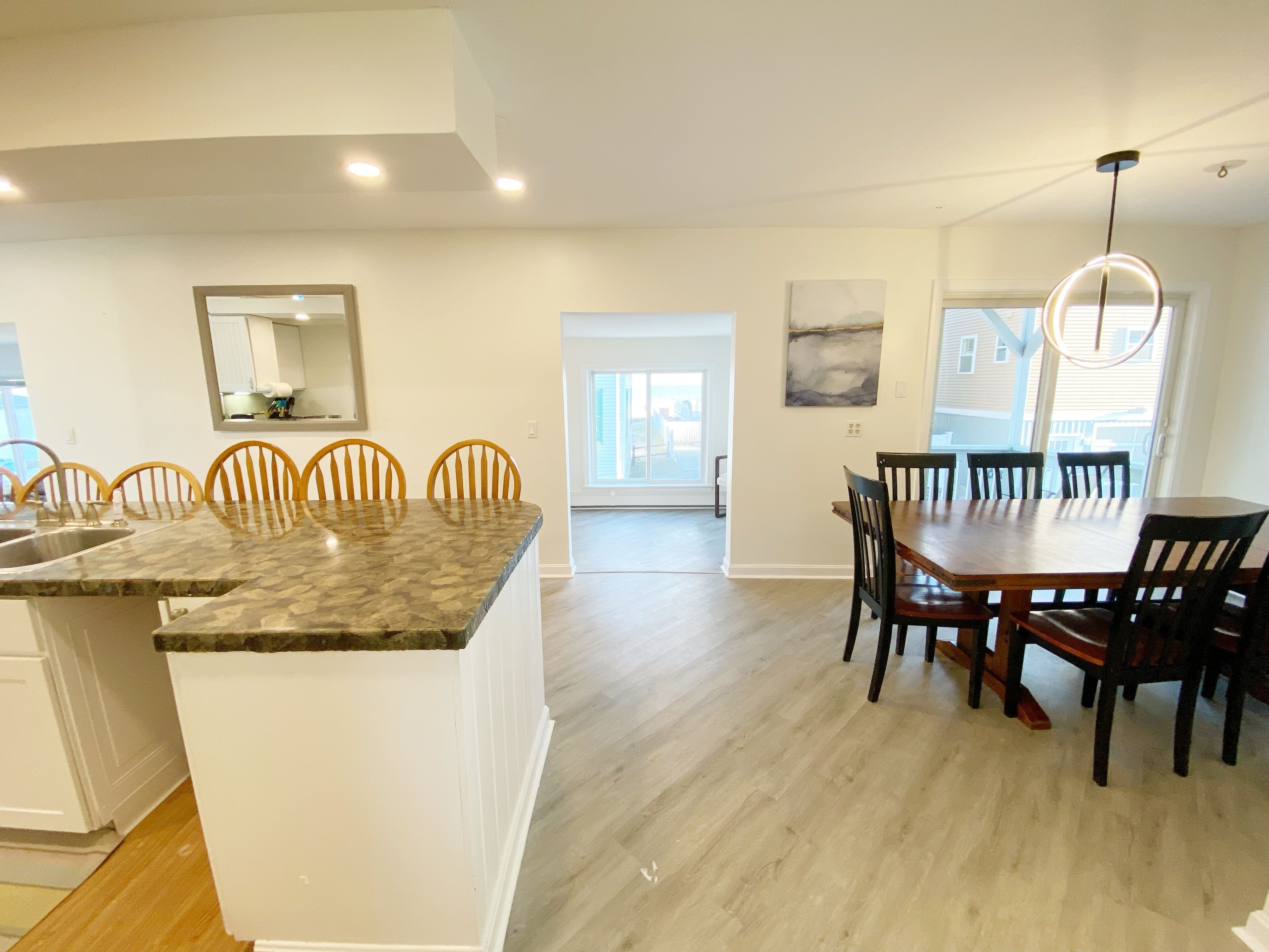 A modern kitchen with a granite countertop, wooden chairs, and a dining table with dark chairs.
