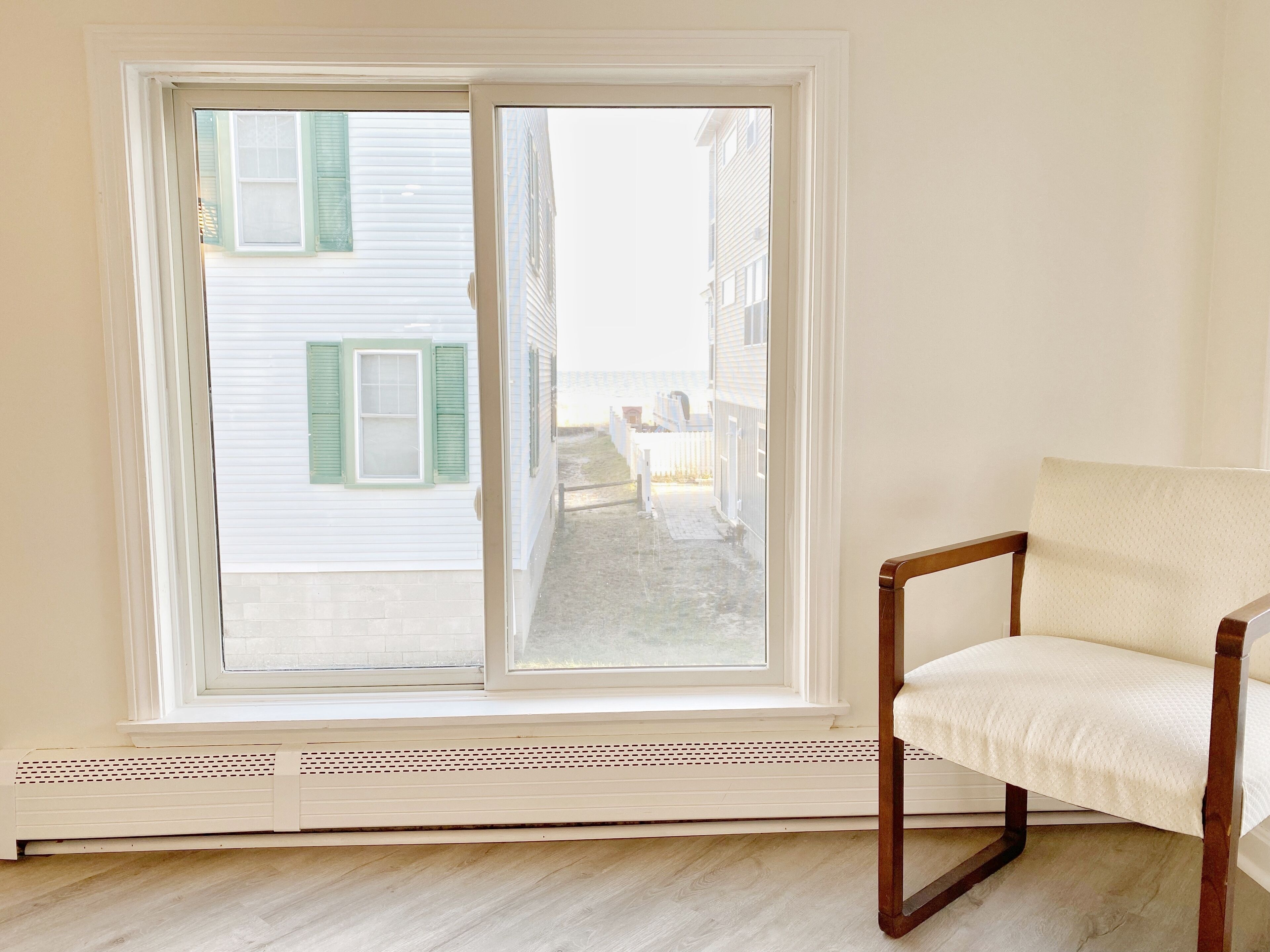 Une pièce avec une grande fenêtre, une chaise en bois et un radiateur blanc.
