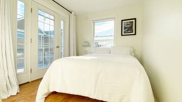 A bedroom with a large bed, a window, and a door leading to a balcony.