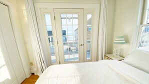 Un dormitorio con una cama grande, una ventana con cortinas, una lámpara y vistas a edificios.