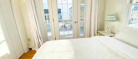 A bedroom with a large bed, a window with curtains, a lamp, and a view of buildings outside.