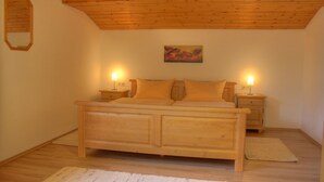 A bedroom with a wooden ceiling, a bed with two nightstands, a painting on the wall, and a rug on the floor. - Ferienwohnung für 5 Personen, 2 Schlafzimmer, 70 m² (Inzell)