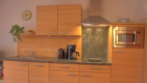 A modern kitchen with wooden cabinets, a stainless steel microwave, and a coffee maker. - Ferienwohnung für 5 Personen, 2 Schlafzimmer, 70 m² (Inzell)