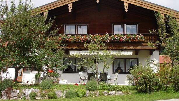 A traditional wooden chalet with a balcony adorned with flowers, a stone pathway leading to the entrance, and outdoor seating. - Ferienwohnung für 5 Personen, 2 Schlafzimmer, 70 m² (Inzell)