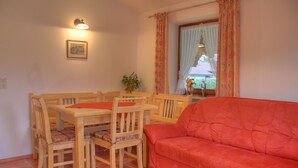 A living room with a wooden dining table, matching chairs, and a red sofa. - Ferienwohnung für 5 Personen, 2 Schlafzimmer, 70 m² (Inzell)