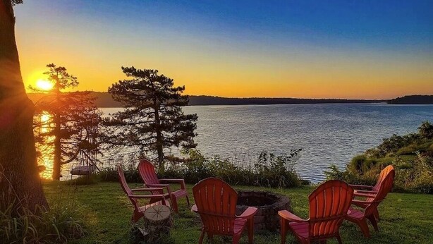 A sunset view over a lake with three Adirondack chairs and a fire pit. - NEW-Waterfront Lodge-Private dock/slip, Kayak, swim, fish, water view from deck (Grove)