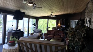 A cozy living room with a wooden ceiling, a large window, a brown leather sofa, and a stone wall decoration. - NEW-Waterfront Lodge-Private dock/slip, Kayak, swim, fish, water view from deck (Grove)