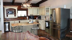 A kitchen with a central island, stainless steel appliances, and a hanging light fixture. - NEW-Waterfront Lodge-Private dock/slip, Kayak, swim, fish, water view from deck (Grove)