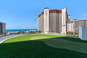 A high-rise hotel with multiple balconies, a well-maintained lawn, and a view of the ocean.