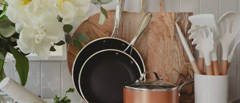 A kitchen counter with a frying pan, a copper pot, a wooden cutting board, and a set of wooden utensils.