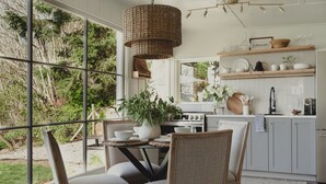 A modern kitchen with large windows, a dining area with chairs, and a hanging light fixture.