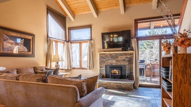 A cozy living room with a stone fireplace, a comfortable sofa, and a television mounted above it.