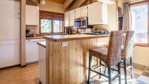 A kitchen with wooden cabinets, a central island with bar stools, and a window with a view of trees.
