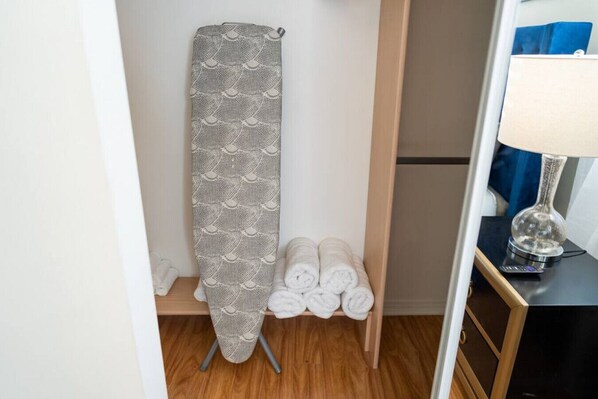 A room with a wooden floor, a towel rack with rolled towels, and a lamp on a side table.