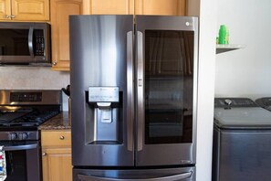 A stainless steel refrigerator with a water dispenser, a microwave, and a stove in a kitchen.