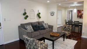 A living room with a grey sofa, patterned armchairs, a coffee table, and a dining area in the background. - 3B/2Bth + Dinning in Historical Tower District (Fresno)