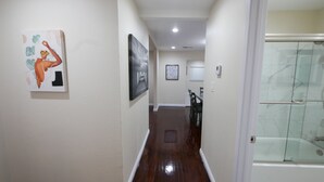 A hallway with artwork on the walls, a glass shower door, and a dining area in the background. - 3B/2Bth + Dinning in Historical Tower District (Fresno)