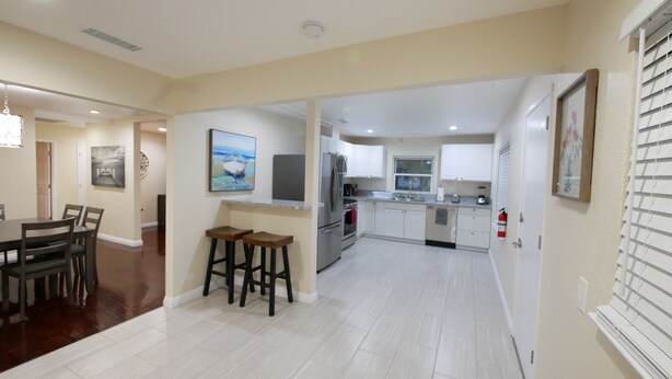 A modern kitchen with white cabinets, stainless steel appliances, and a dining area with a wooden table and chairs. - 3B/2Bth + Dinning in Historical Tower District (Fresno)