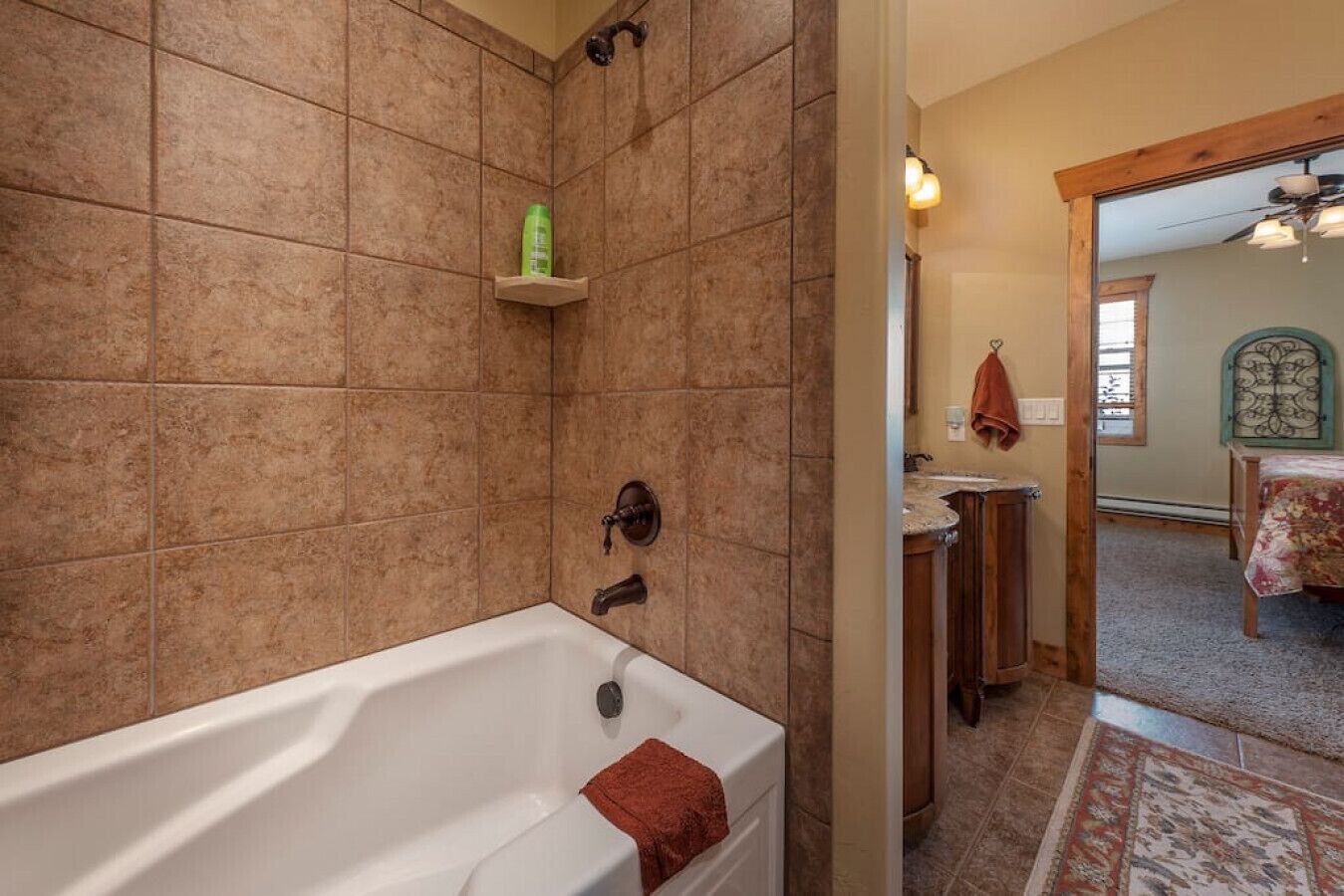 A bathroom with a bathtub, a shower, and a sink. There is a shelf with toiletries and a towel hanging on the wall.