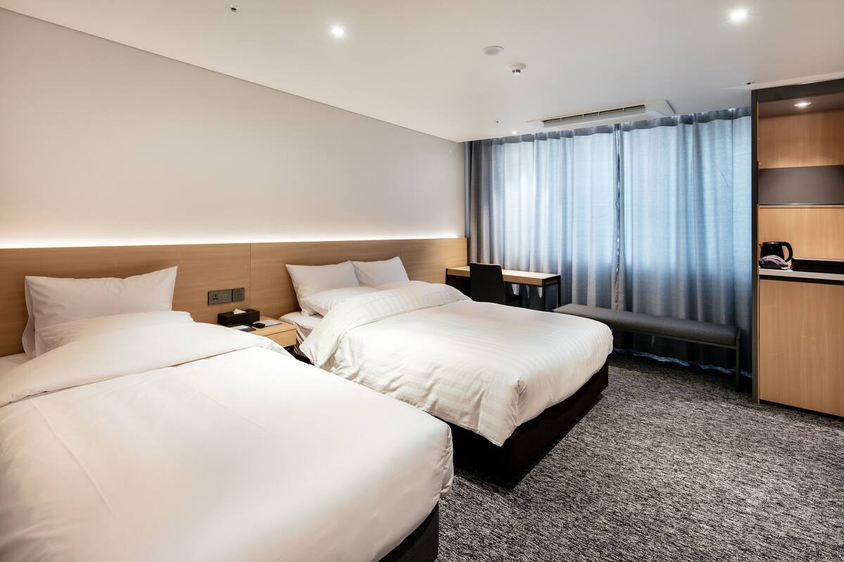 Una habitación de hotel con dos camas, un escritorio, una silla, una cafetera y una ventana con cortinas.