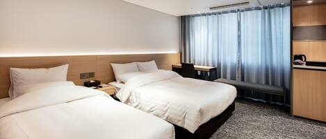 A hotel room with two beds, a desk, a chair, a coffee maker, and a window with curtains.
