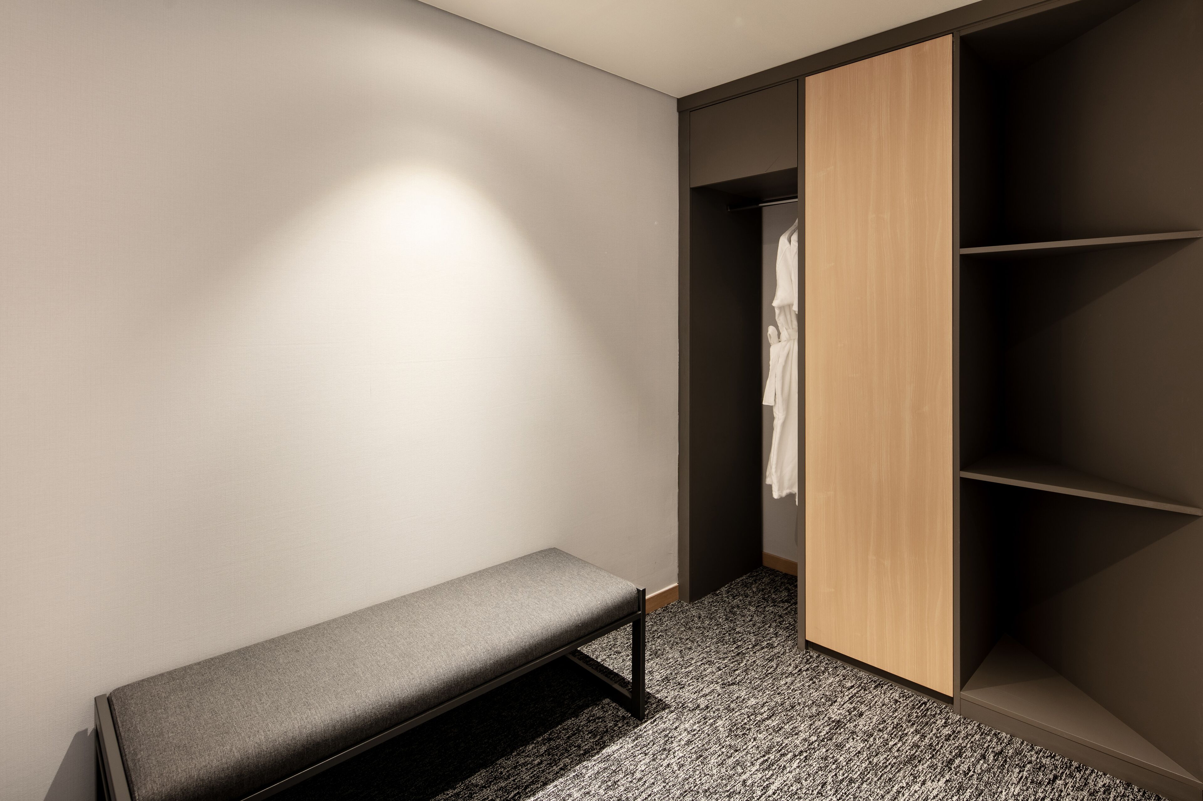 Ein moderner, minimalistischer Raum mit einer Bank, einem Holzschrank und hängender Kleidung darin.