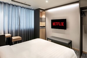 A hotel room with a bed, a desk, a bench, a wardrobe, and a wall-mounted TV displaying the Netflix logo. - Icheon Sky Sun Hotel (Icheon)