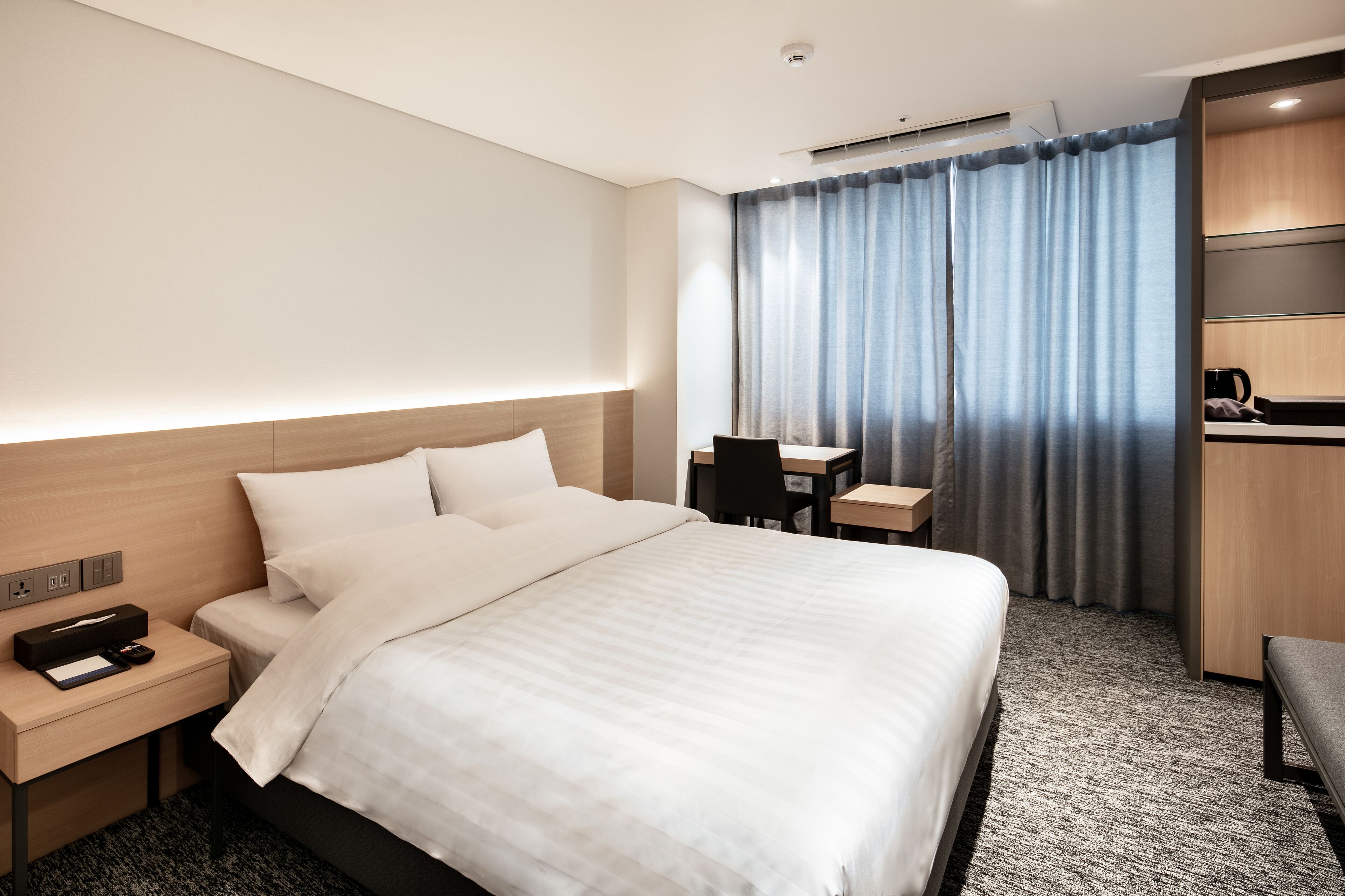 A hotel room with a large bed, a desk, a chair, and a small table with a coffee maker.