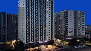 Un hotel moderno de rascacielos con una fachada de ventanas en cuadrícula, una entrada destacada y un paso de peatones enfrente.