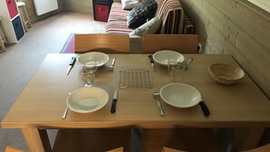 A dining table set with plates, cutlery, and glasses, surrounded by wooden chairs in a room with a sofa and a radiator.