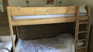 A bunk bed with a wooden headboard, a ladder on the right side, and a single bed on the left.